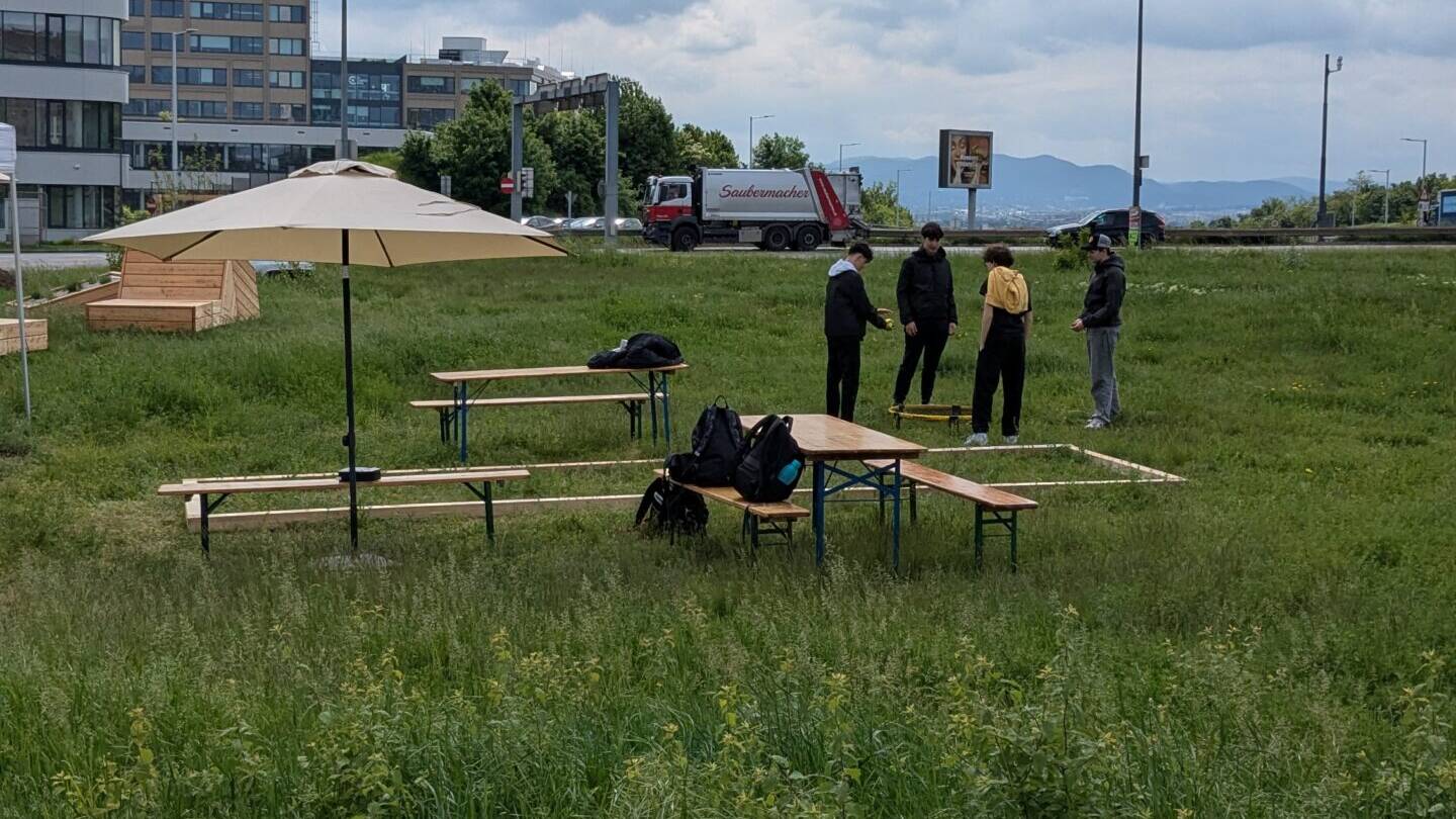 Heurigengarnituren und Schirm auf Wiese mit Blick auf Autos am Verteilerkreis